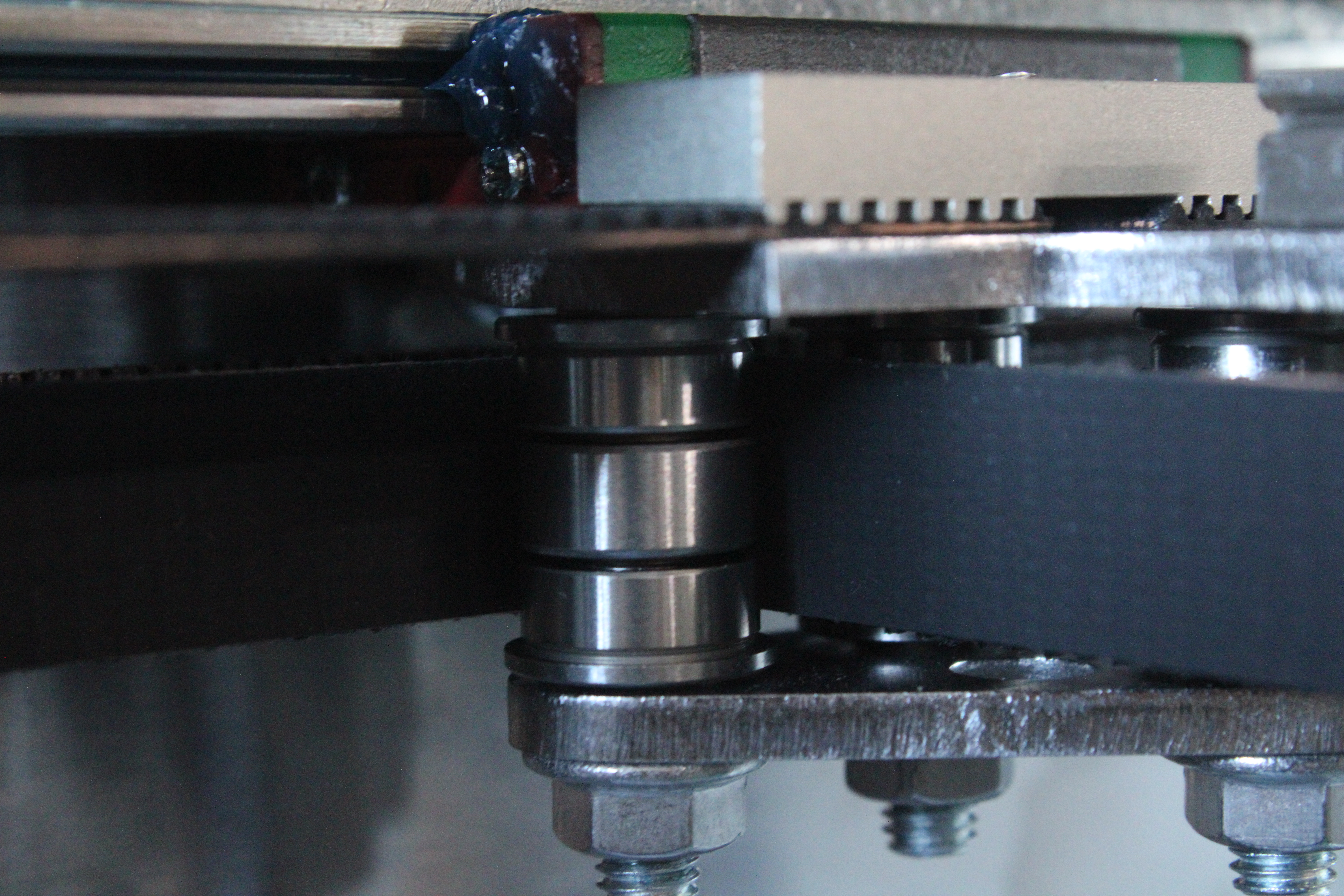 Close-up of a crossbar belt roller on the T0 side: a stack of three bearings with washers between them and the belt running around it