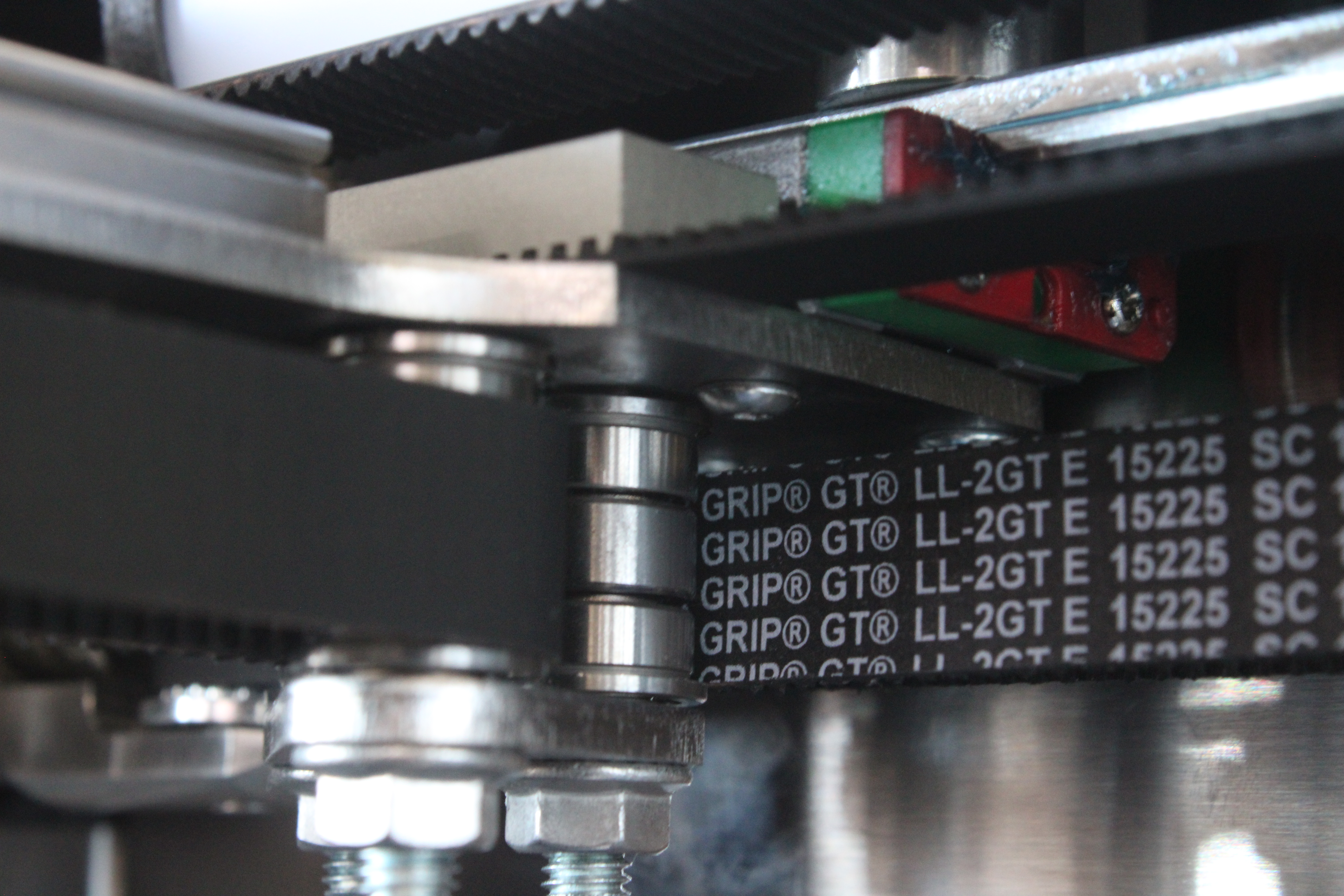 Close-up of a crossbar belt roller on the T1 side: a stack of three bearings with washers between them and the belt running around it
