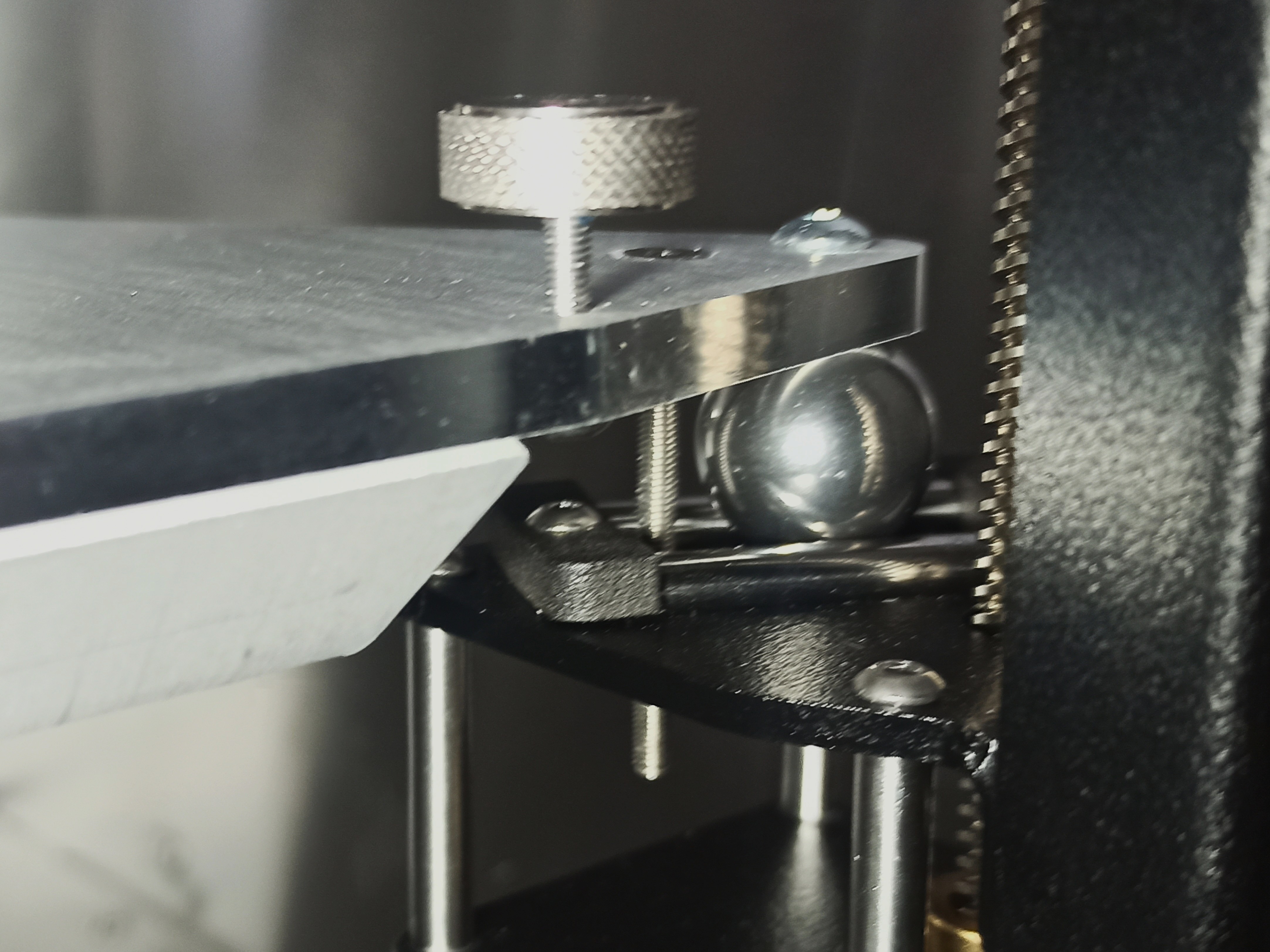 Close-up of an installed build plate securing screw. The countersunk M3 screw passes through the build plate and threads into the holder, secured from the bottom with a nut.