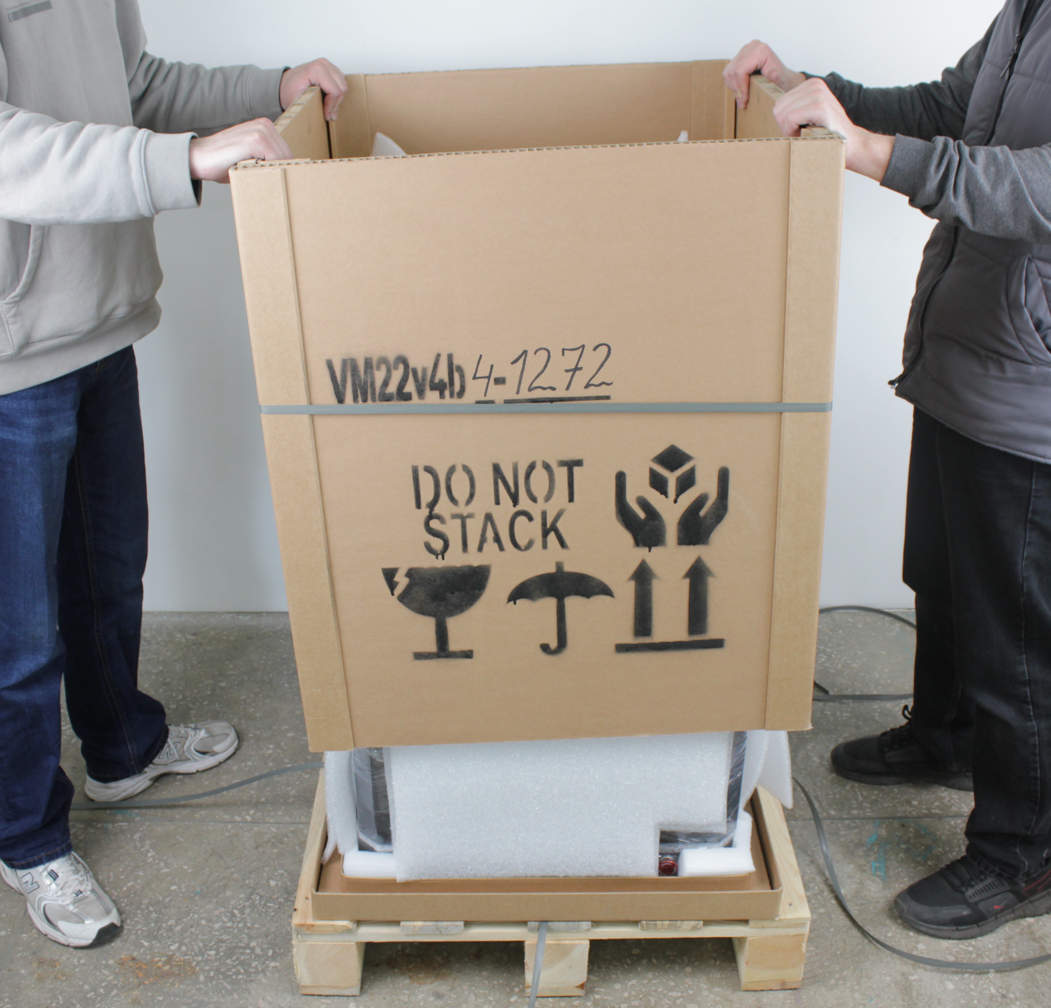 Two people lifting outer crate box vertically and removing foam packing